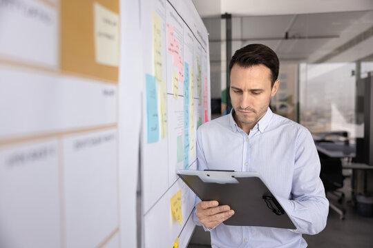 Business project analysis. Serious mid adult man market analyst operations manager review data on paper clipboard compare update information with workflow structure on agile planning board. Copy space