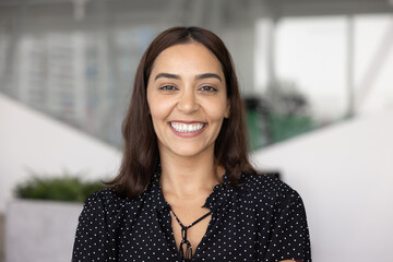Happy beautiful Middle Eastern businesswoman posing for head shot with toothy smile, looking at camera, laughing, standing for picture in office. Positive young professional, CEO, executive portrait © fizkes