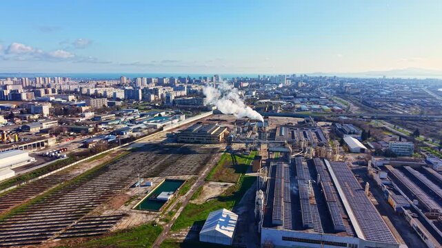 A view of an industrial zone in a city with buildings, factories, and smoke billowing into the sky. The scene shows a mix of urban development and open land.