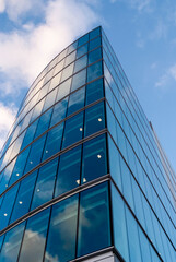 Obraz premium Modern glass facade reflecting blue sky and white clouds