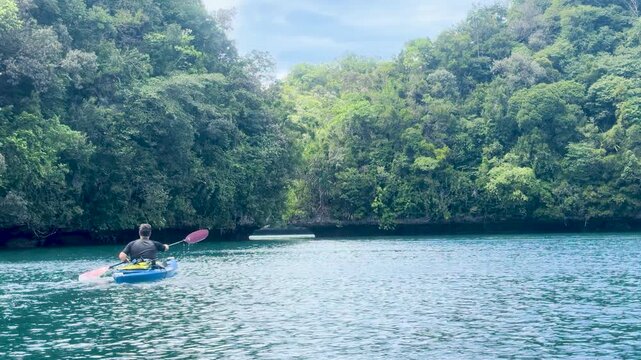Man Paddling Blue Kayak Through Tropical Rock Islands in Palau Lagoon