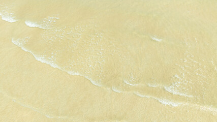Top view show waves crashing onto a tropical coastline with crystal-clear blue waters contrasting with sandy beaches and coral reefs off the shore of a tropical island with emerald-green waters.