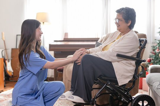 Nurse holding hands with senior woman in wheelchair at home, providing compassionate healthcare support. Elderly care service, rehabilitation assistance and trusted medical caregiver concept.
