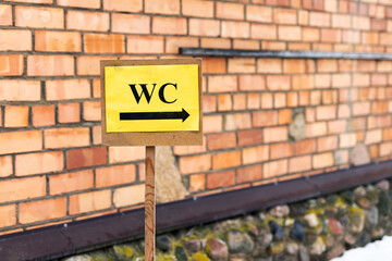Dusty outdoor restroom indicator attached to brick wall in wintery city environment