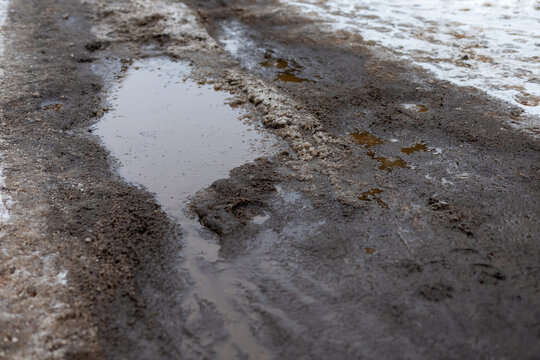 Snowmelt mud hints road. Overcast scene with puddles and tire track marks visible