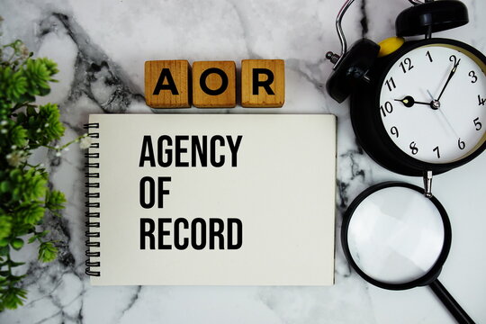 AOR Agency of Record text with alarm clock and magnifying glass on marble background