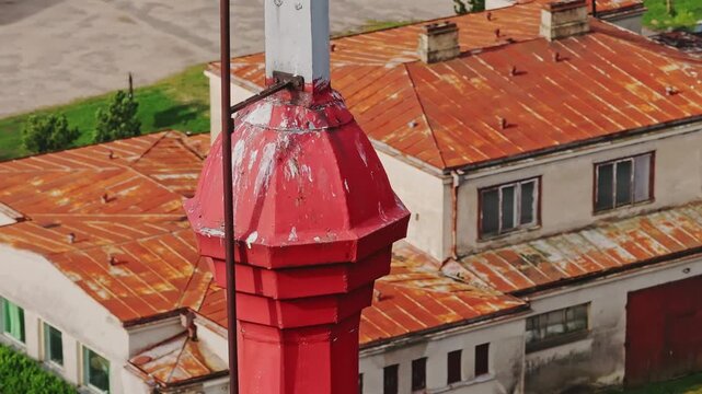 Close aerial of white crucifix crowning chapel tower above rusted roofs