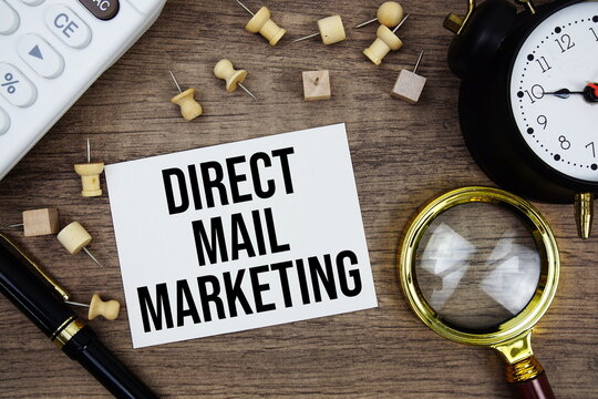 Direct Mail Marketing text written on notepad with pen, alarm clock, magnifying glass and calculator on wooden background