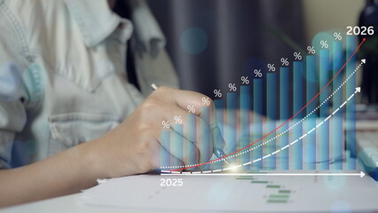 Business financial growth concept with rising bar chart and upward trend line from 2025 to 2026. Analyst hand writing on report, investment planning, profit increase, revenue forecast, 