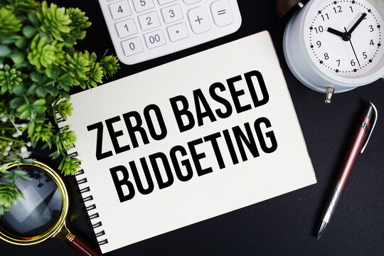ZBB Zero Based Budgeting text written on notepad with alarm clock, magnifying glass and calculator on black background
