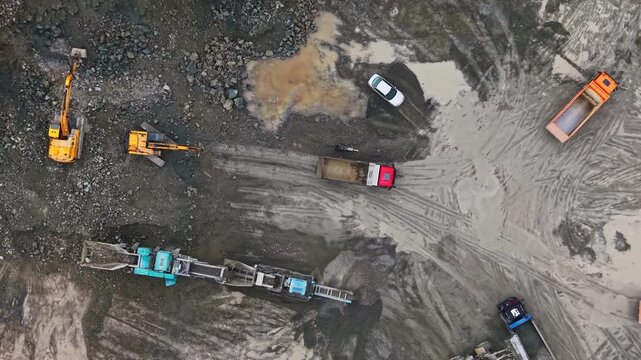 Heavy machinery and trucks work at a granite quarry site. Excavators, loaders, and transport vehicles are active as workers manage stone extraction and material movement.