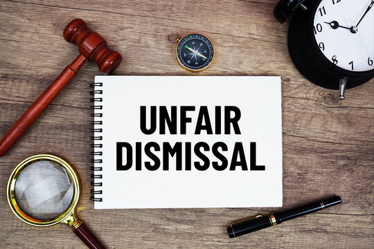 Unfair Dismissal message written on notepad with alarm clock, wood gavel and magnifying glass flat lay on wooden background