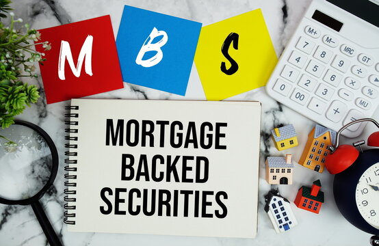 MBS Mortgage-Backed Securities text written on notepad with house model, magnifying glass, calculator and alarm clock on marble background