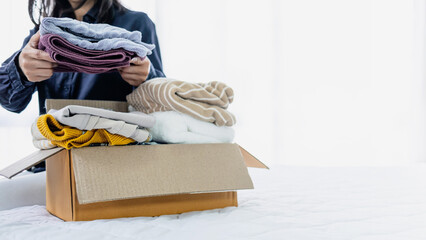 Woman placing folded clothes into a cardboard box for donation. Concept of charity, clothing donation, recycling and sustainable living.