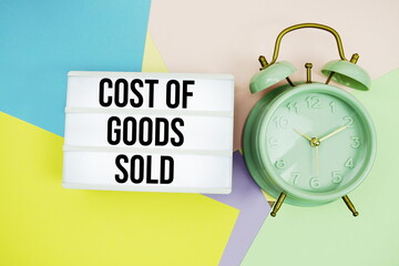 Cost of Goods Sold text in lightbox with alarm clock on pastel background