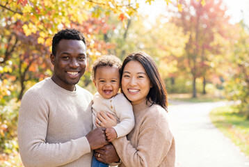 Fototapeta premium Happy diverse family with a baby smiling together in an autumn park