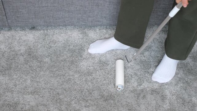 A woman removes dirt from a carpet using mop with a lint roller.