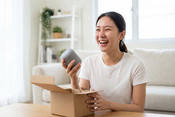 Happy asian woman laughing while unboxing a new smart speaker from a delivery package