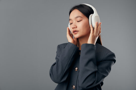 Woman with eyes closed wearing headphones and dark jacket listening to music or podcast in studio. Relaxation, audio, technology, and focus with casual outfit and minimal background.