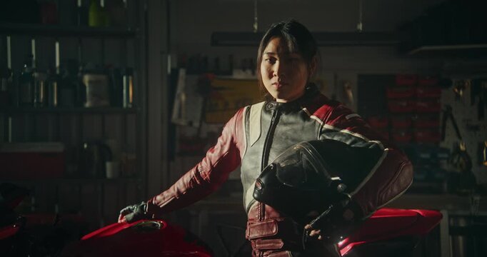 Young Asian Woman Standing Confidently Beside Red Sports Motorcycle. Clad in Professional Red and Black Leather Riding Suit, Girl Holds Helmet Under One Arm. Concept of Self Empowerment and Identity.