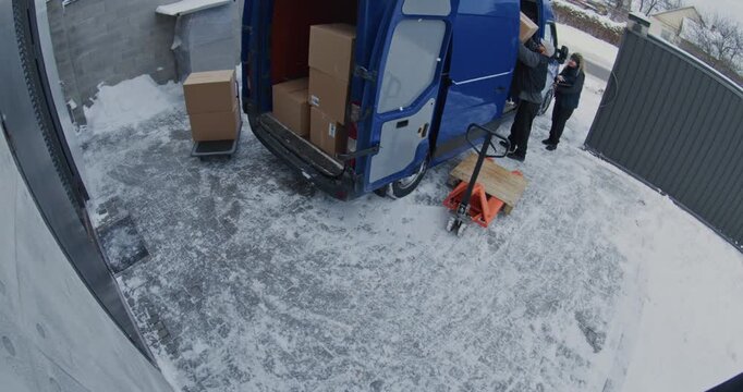 Team Loads Cardboard Boxes From Warehouse Into Van. Man Moves Parcels Using Pallet Jack And Trolley While Woman Scans Inventory With Tablet. Concept CCTV, Professional Logistics Process. Timelapse.