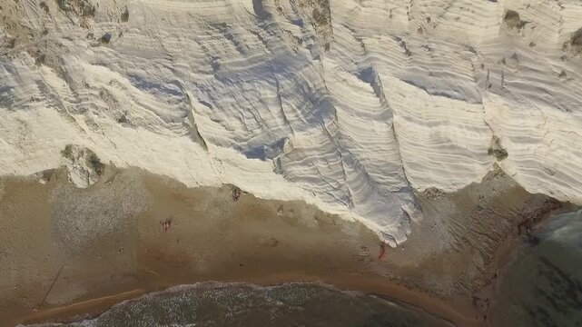 Aerial overhead view of Scala dei Turchi white cliffs meeting sandy beach and turquoise sea in Sicily, Italy, with few distant figures, dramatic coastal landmark.
