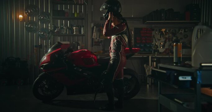 Focused and Determined Asian Woman in Professional Leather Riding Suit Prepares For High Speed Ride Inside Modern Workshop. Female Carefully Puts on Helmet and Pulls on Sleek Black Leather Gloves.