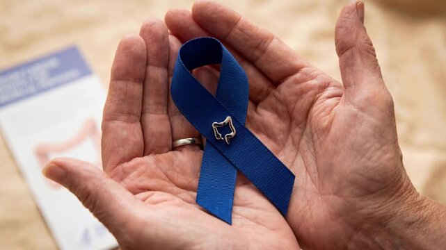 Blue ribbon awareness for colorectal health held in elderly hands, holding and supporting screening, medical diagnostic support and emotional hope