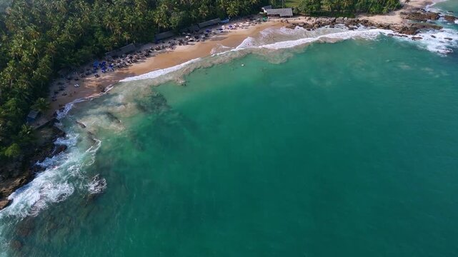 Aerial view of Goyambokka Beach in Tangalle, Sri Lanka, lined with many sunbeds and umbrellas. A popular tropical holiday destination with golden sand and turquoise ocean.