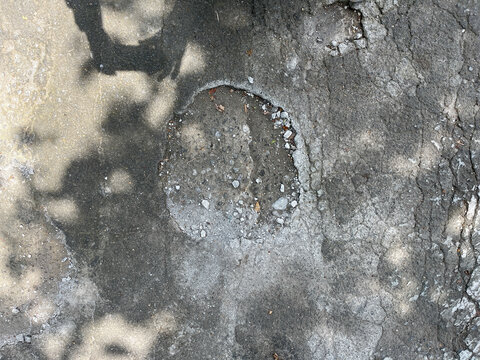 A grey concrete surface with a hole in the middle. The hole is surrounded by gravel and dir