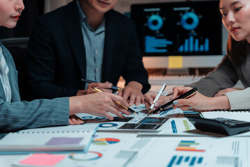 Business people collaborating, analyzing financial data charts and graphs from documents and a monitor, working late in an office © Crystal