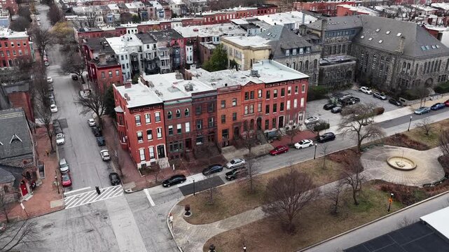Aerial view of Baltimore&rsquo;s Bolton Hill neighborhood in winter, with historic brick townhouses, a large stone church and quiet residential square with leafless trees and parked cars. Approaching shot.