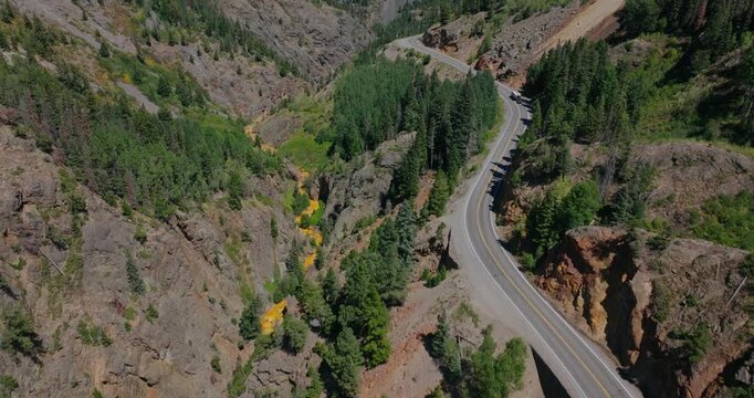 Aerial of winding alpine highway cutting by rugged forested Colorado mountains, Million Dollay Highway Colorado USA