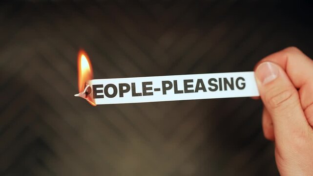 Close-up of hand burning a paper label that says &ldquo;people-pleasing,&rdquo; symbolizing setting boundaries, self-growth, and breaking unhealthy habits with copy space.