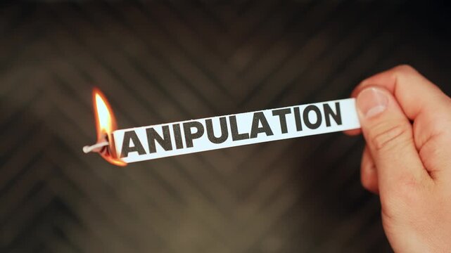 Close-up of a hand holding a paper label reading &ldquo;MANIPULATION&rdquo; as the edge burns in flame, symbolizing toxic control, gaslighting, and breaking free.