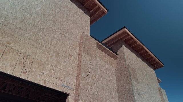 Steady upward pan of new home framed in plywood beneath bright blue sky.