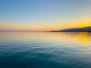 Obraz premium Scenic sunset over Issyk Kul Lake in Kyrgyzstan. The sun sets behind the mountains, casting a golden reflection across the water.
