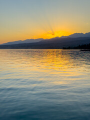 Fototapeta premium Scenic sunset over Issyk Kul Lake in Kyrgyzstan. The sun sets behind the mountains, casting a golden reflection across the water.