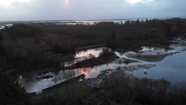 A cinematic aerial view of the Lough Corrib coastline in Cong, County Mayo, featuring calm waters, small boats, and a dramatic sunset reflection. Perfect for travel and nature documentaries.