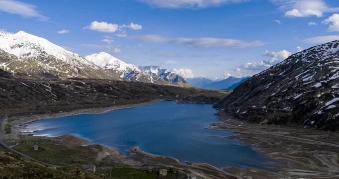 Montespluga lake reflecting blue sky surrounded by snowy Alps mountains in Italy. Aerial Hyperlapse