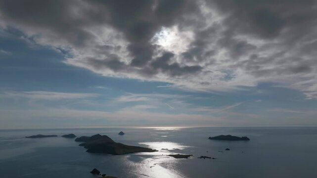 Dramatic aerial shot of the Great Blasket Island in Ireland, featuring sun rays breaking through thick clouds over the Atlantic Ocean.