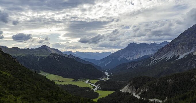 Aerial Hyperlapse of Fuorn Pass or Ofen Pass a high alpine mountain pass in Graub&uuml;nden Switzerland A dramatic cloudy sky and rugged mountain landscape with a river flowing through the valley.