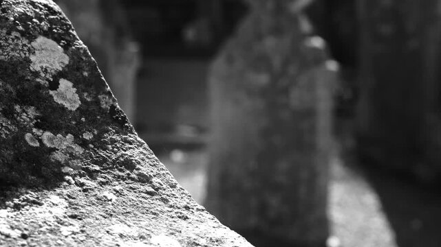 A moody infrared closeup of a weathered carved stone in a cemetery, featuring an ancient headstone out of focus in the background. Ideal for historical or spooky themes.