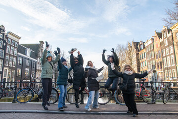 Group of excited mature women friends jumping on a canal bridge in amsterdam, celebrating vacation and freedom with happiness during a european city trip