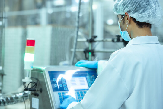 Factory machine operator checks production data on touch screen panel in food manufacturing plant, representing automation system management and regulatory compliance process.