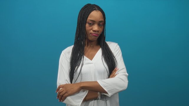 Woman with arms crossed and hands visible in a studio setting with blue backdrop and guarded side glance; skepticism.