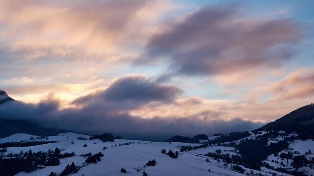 Winter mountain timelapse of clouds rolling over snowy peaks and forest during sunset