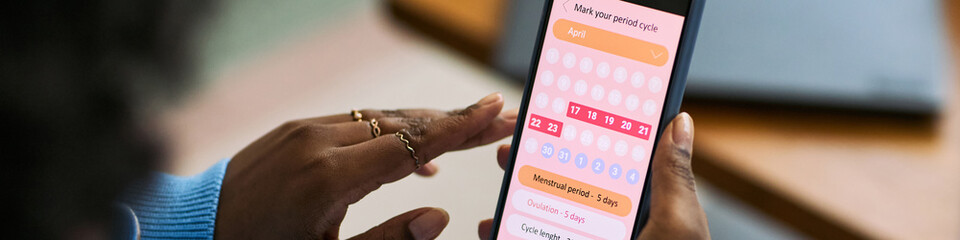 Black woman using smartphone tracking menstrual cycle with femtech health app, hand interacting with digital calendar interface, focusing on period and ovulation dates