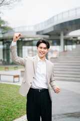 Fototapeta premium Confident Asian entrepreneur showing victory gesture outdoors, business success, leadership mindset, motivation, ambition and corporate career growth concept.