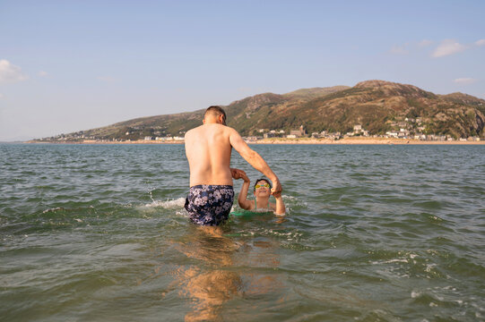 Father teaching daughter to swim in shallow sea water.